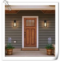 the front door of a house with two planters on the porch and one light on