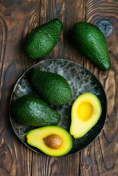 an avocado cut in half on a plate with two halves and one whole