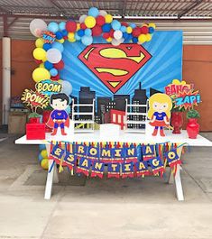 a table topped with balloons and decorations for a superman themed birthday party in a garage