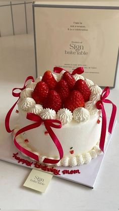 a white cake with strawberries on top and ribbon around the edges, sitting in front of a sign