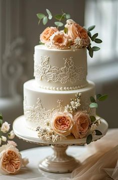 a three tiered wedding cake with peach flowers on top and greenery around the edges