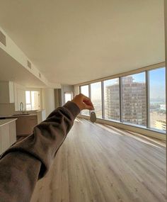 a person's hand reaching out towards an empty room with large windows and wood flooring