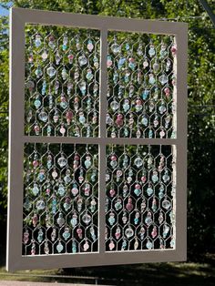 a metal screen with many different colored glass beads on it and trees in the background