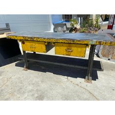 an old workbench with yellow drawers is sitting on the concrete in front of a garage