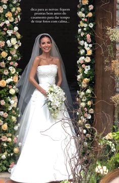 a woman in a wedding dress standing next to a flower arch