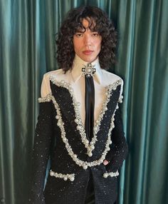 a man with curly hair wearing a black and white suit, neck tie and pants