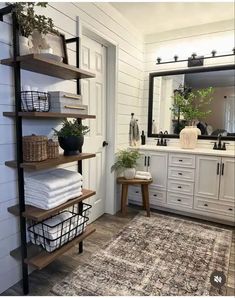 a bathroom with white walls and wooden shelves filled with towels, plants and other items