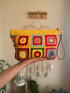 a hand holding a yellow crocheted purse with multicolored squares on it