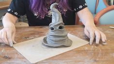 a woman is making a vase out of clay on a wooden table with purple hair