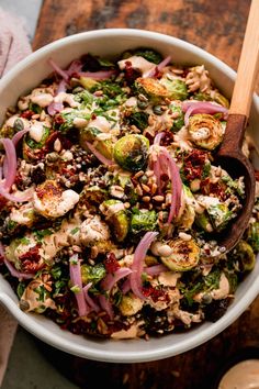 a white bowl filled with salad on top of a wooden table next to a spoon