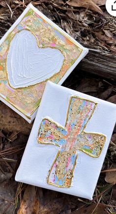 two cross shaped coasters sitting on the ground next to leaves and twigs, one with a heart cut out of it