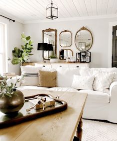 a living room with white furniture and mirrors on the wall above the coffee table is decorated with greenery