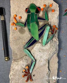 a green frog sitting on top of a rock next to an orange and black marker