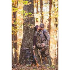 a couple kissing in the woods next to a tree with their hunting gear on it