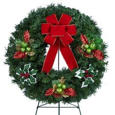 a christmas wreath with red bow and green ornaments on it, sitting on a stand