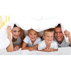 a family is under the covers on their bed smiling at the camera while laying down