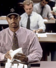 a man sitting at a desk with papers in front of him and other people behind him