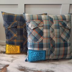 two plaid pillows sitting on top of a wooden table next to each other, one blue and the other gray