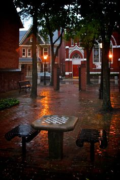 two park benches sitting in the middle of a rain soaked street with lights shining on them