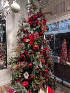 a christmas tree decorated with red ornaments and greenery in a store window display case