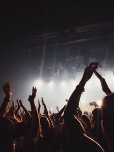 a crowd of people at a concert with their hands in the air and lights on