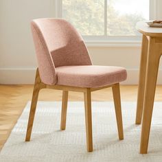 a pink chair sitting next to a wooden table on top of a white area rug