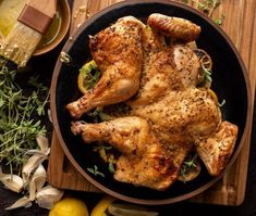 chicken with lemons and herbs on a black plate next to some seasoning, butter and garlic