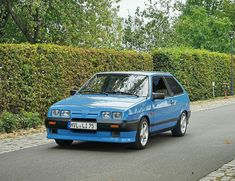 a blue car parked on the side of a road next to a hedge covered street