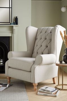 a living room with a white chair and some books on the floor next to a fire place