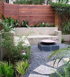 an outdoor garden with stone benches, plants and graveled walkway leading to a wooden fence