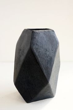 a black vase sitting on top of a white table next to a gray and black object