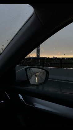 the rear view mirror of a car with rain on it's windshield and street lights in the background