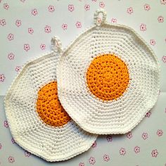 two crocheted fried eggs are sitting on a pink and white tablecloth with flowers in the background