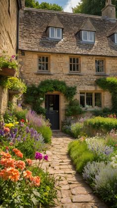 an old stone house with lots of flowers in the front yard and walkway leading up to it