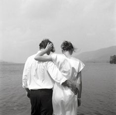 a man and woman standing next to each other near the water with their arms around each other