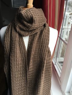 a brown knitted scarf sitting on top of a white mannequin next to a window