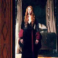 a woman with long red hair standing in front of a bed