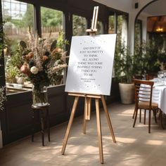 an easel with a sign on it in front of some tables and chairs at a restaurant