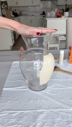 a woman's hand reaching into a large glass vase on top of a table