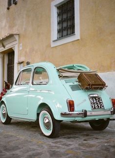 an old car is parked in front of a building with luggage on the roof and a woman's purse next to it