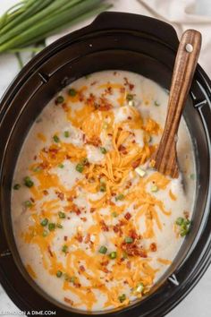 a crock pot filled with cheesy potato soup and topped with green onions