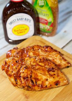 two pieces of chicken sitting on top of a cutting board next to a jar of bbq sauce