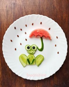 a white plate topped with cut up vegetables and an alien holding an umbrella on top of it