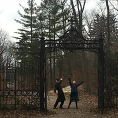 two people standing in front of an iron gate with their arms up and one person reaching for the frisbee