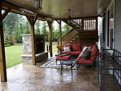 a covered patio with red couches and chairs on the front porch next to an outdoor fireplace