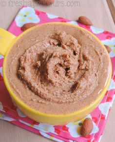 a yellow bowl filled with peanut butter on top of a pink and white napkin next to nuts