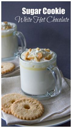 two mugs filled with white hot chocolate and topped with whipped cream next to cookies