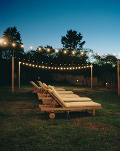 a row of lounge chairs sitting on top of a lush green field next to lights