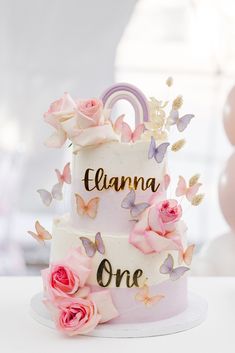 a three tiered cake with pink flowers and butterflies on the top is decorated with nameplates