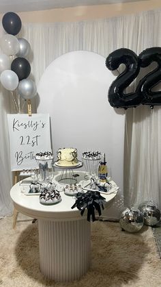 a white table topped with lots of cake next to black and silver balloons in the shape of numbers